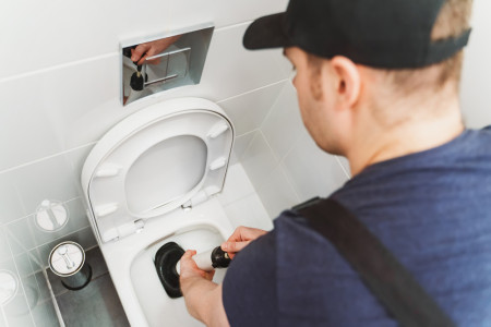 Plumber unclogging toilet with force pump cleaner
